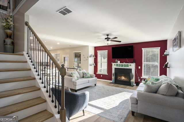 living area featuring visible vents, a fireplace with flush hearth, wood finished floors, and stairway