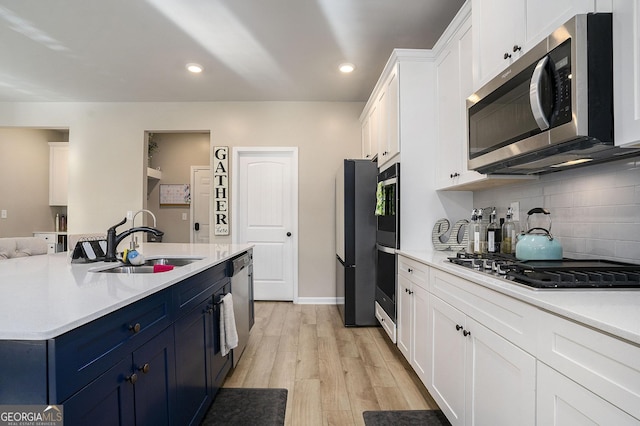 kitchen with light wood-type flooring, a sink, blue cabinetry, stainless steel appliances, and white cabinets