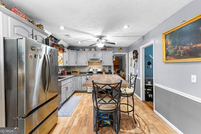 kitchen with a ceiling fan, baseboards, light wood finished floors, appliances with stainless steel finishes, and backsplash