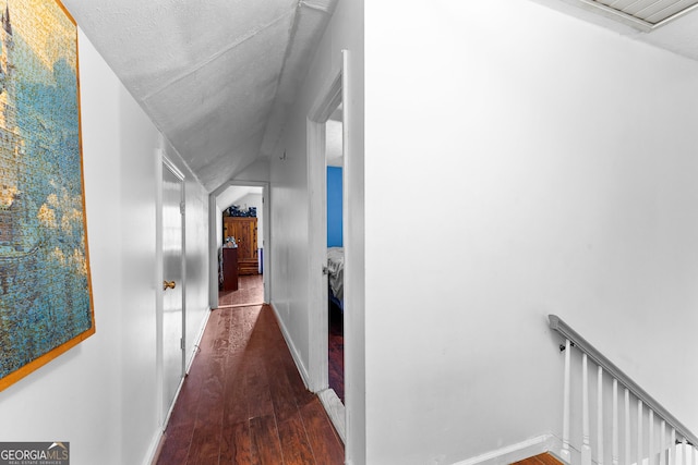 corridor featuring baseboards, an upstairs landing, wood finished floors, and vaulted ceiling