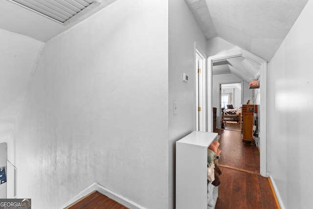 hall featuring visible vents, baseboards, dark wood-style flooring, vaulted ceiling, and a textured ceiling