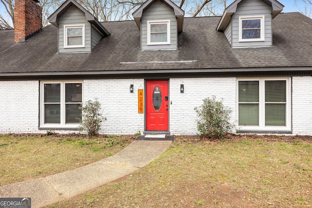 new england style home featuring brick siding, roof with shingles, and a front yard