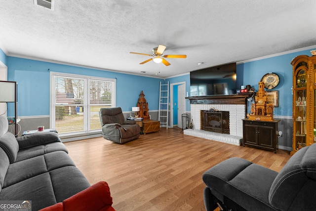 living area featuring ornamental molding, a ceiling fan, a textured ceiling, wood finished floors, and a fireplace