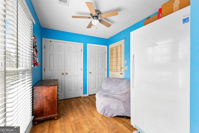 bedroom featuring wood finished floors, visible vents, freestanding refrigerator, ceiling fan, and a closet