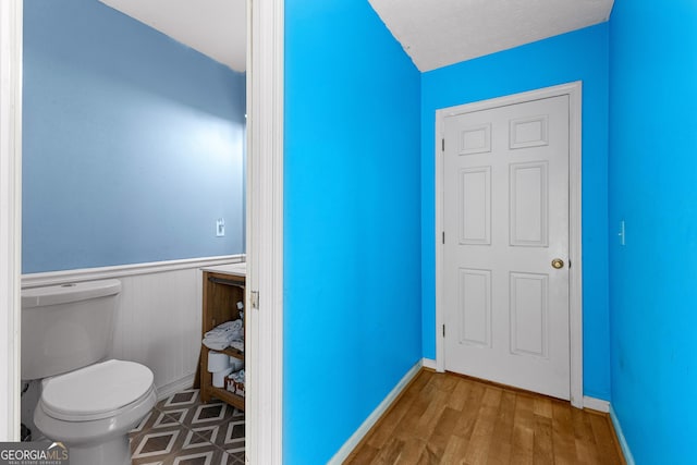 bathroom with toilet, wood finished floors, and wainscoting