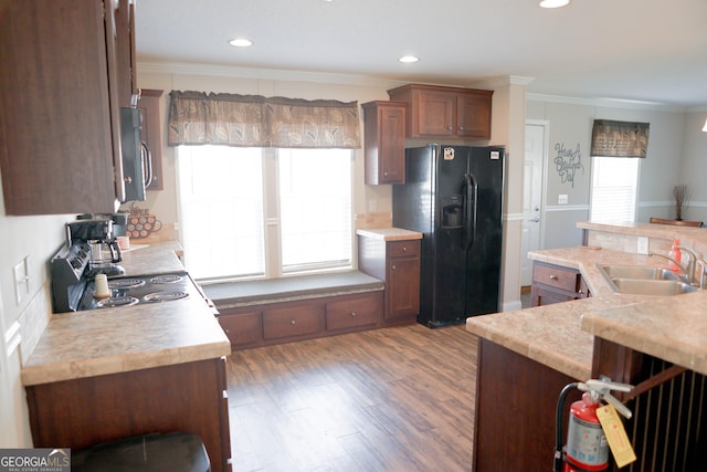 kitchen featuring ornamental molding, a sink, stainless steel microwave, light countertops, and black refrigerator with ice dispenser