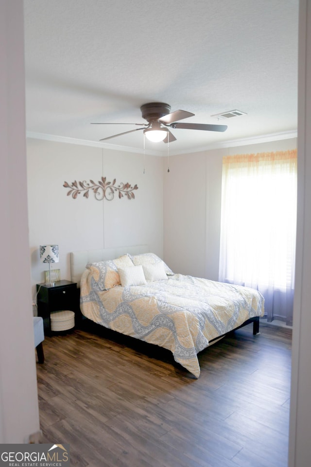 bedroom with ceiling fan, visible vents, wood finished floors, and ornamental molding