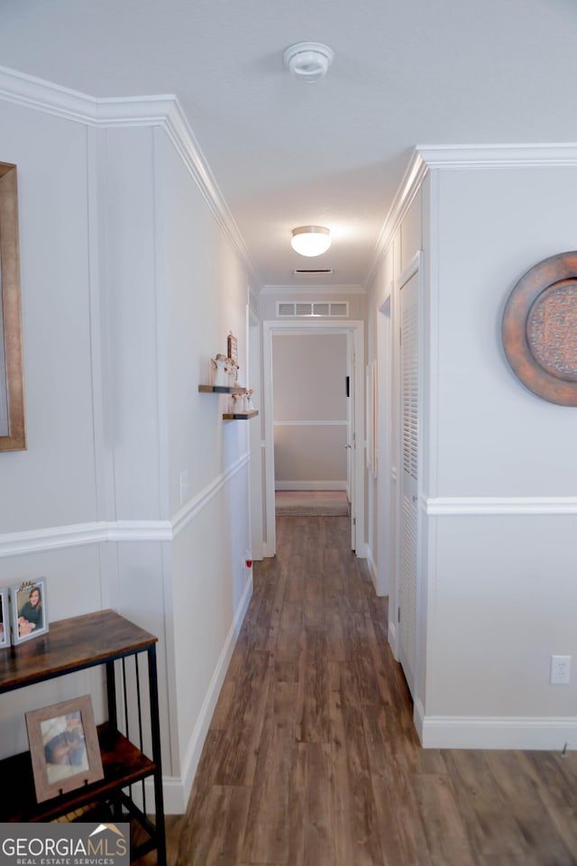 hallway with crown molding, wood finished floors, visible vents, and baseboards