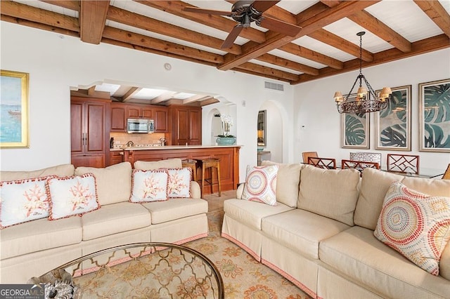 living area featuring visible vents, coffered ceiling, beam ceiling, arched walkways, and ceiling fan with notable chandelier