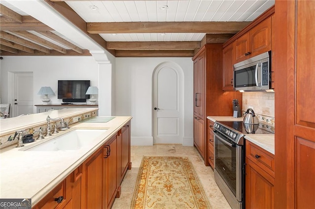 kitchen with light countertops, decorative backsplash, brown cabinetry, stainless steel appliances, and a sink