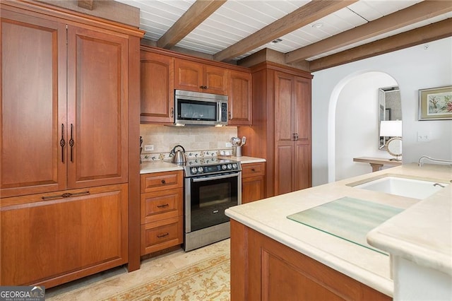 kitchen with arched walkways, light countertops, appliances with stainless steel finishes, brown cabinets, and backsplash