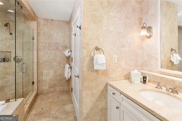 full bath with stone tile flooring, a shower stall, tile walls, and vanity