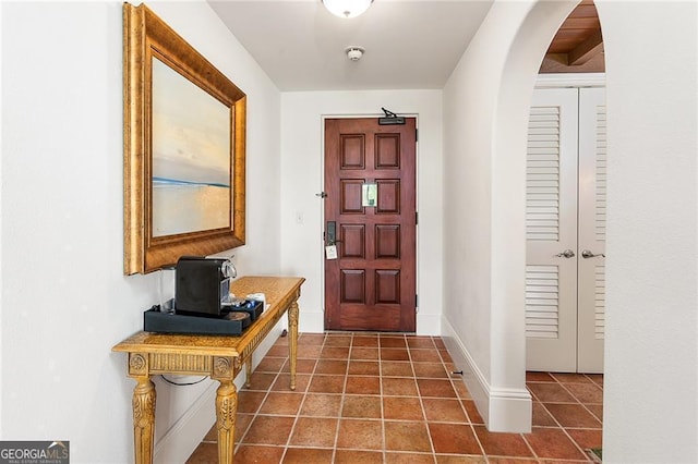 entryway featuring baseboards, arched walkways, and dark tile patterned flooring