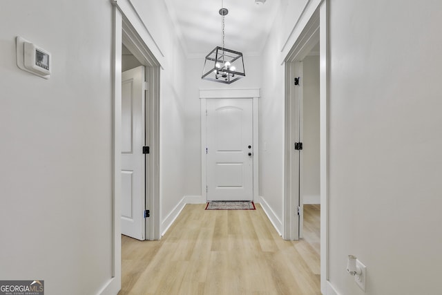 doorway to outside with a chandelier, crown molding, light wood-type flooring, and baseboards