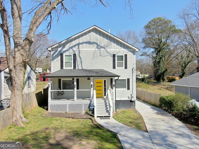 view of front facade with board and batten siding, a porch, a front lawn, and fence