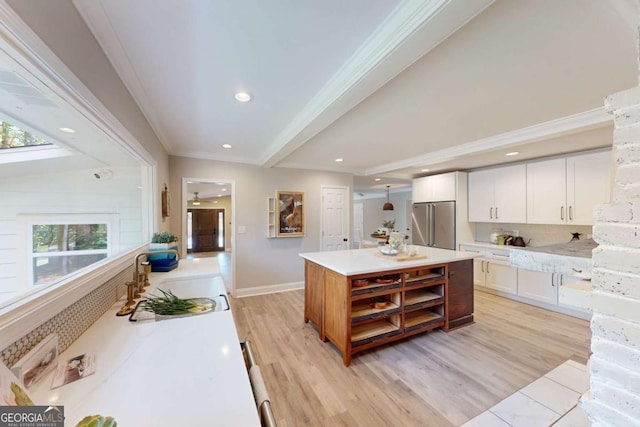 kitchen with light wood finished floors, high end fridge, ornamental molding, a sink, and white cabinetry