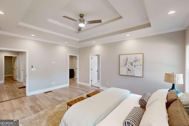 bedroom featuring light wood-type flooring, visible vents, ornamental molding, a tray ceiling, and baseboards