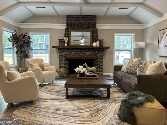 living room featuring vaulted ceiling, a brick fireplace, wood finished floors, and visible vents