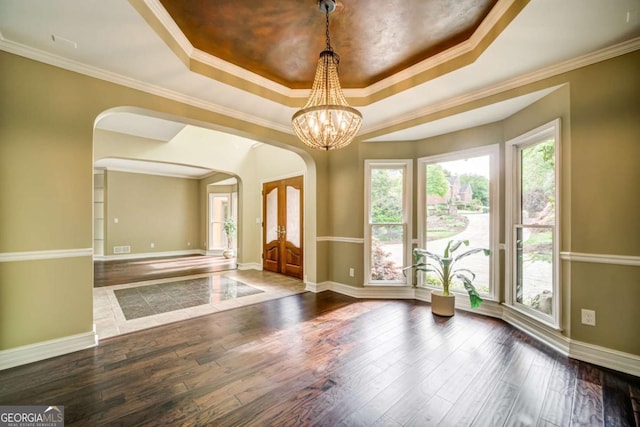 interior space with arched walkways, crown molding, a raised ceiling, and hardwood / wood-style flooring