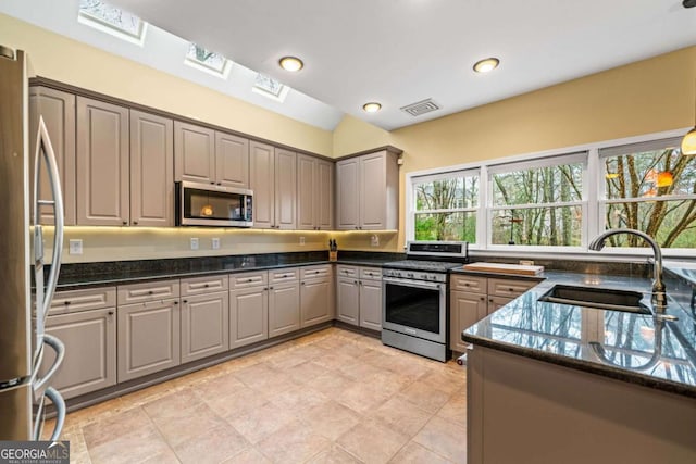 kitchen featuring gray cabinets, a sink, dark stone countertops, stainless steel appliances, and a skylight