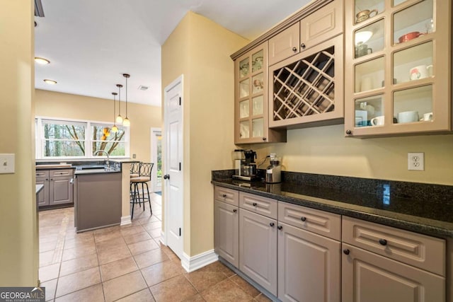 kitchen featuring light tile patterned floors, baseboards, dark stone counters, hanging light fixtures, and glass insert cabinets