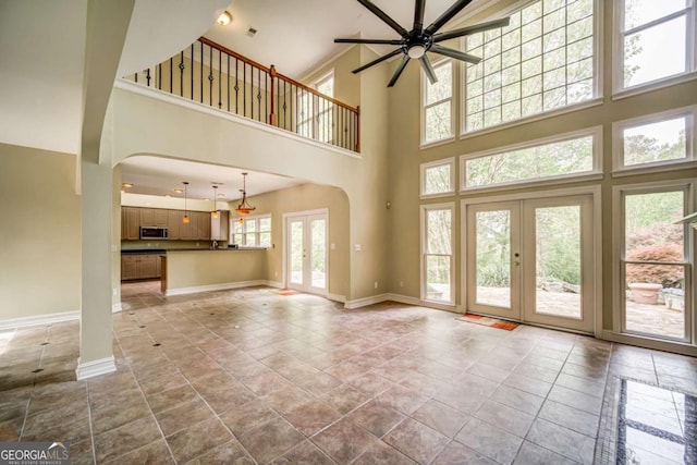 unfurnished living room with french doors, arched walkways, baseboards, and a ceiling fan