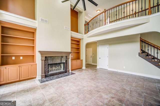 unfurnished living room with a high end fireplace, visible vents, ceiling fan, baseboards, and stairs