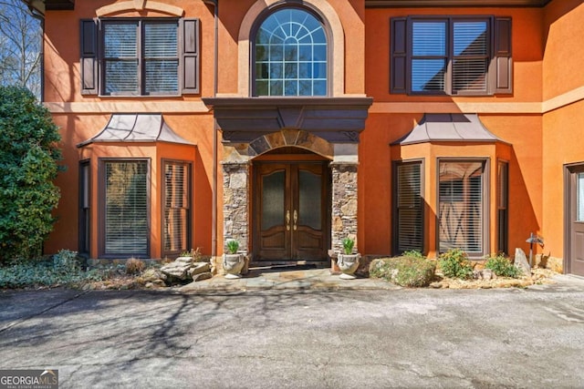 entrance to property featuring french doors, stone siding, and stucco siding