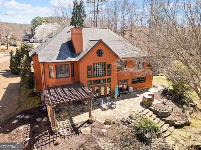 back of house with stucco siding, a patio area, roof with shingles, and a chimney