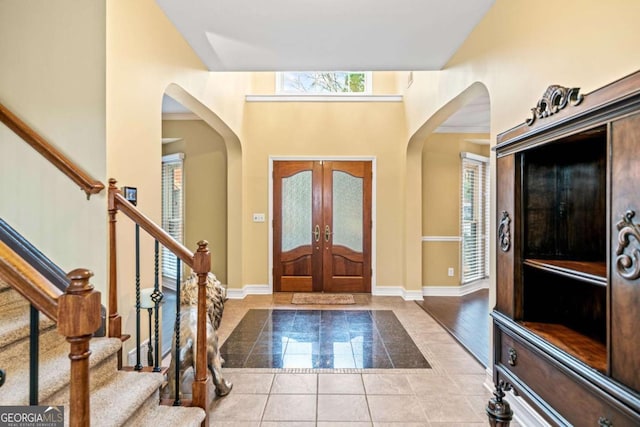 foyer entrance with tile patterned floors, baseboards, stairs, french doors, and arched walkways