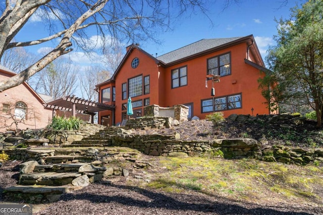 rear view of property with stucco siding and a pergola