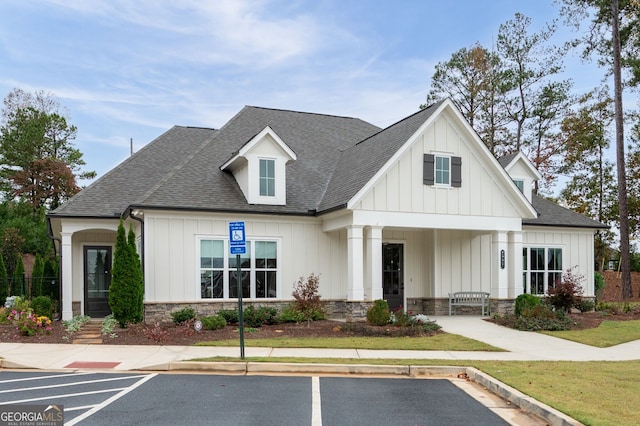 modern inspired farmhouse with uncovered parking, stone siding, roof with shingles, and board and batten siding