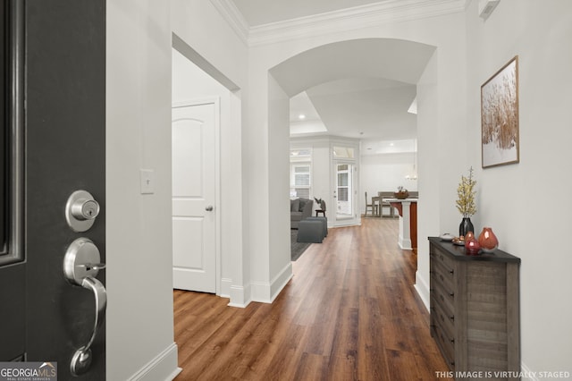 hallway with crown molding, wood finished floors, arched walkways, and baseboards