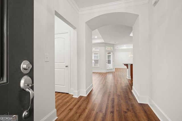 corridor with baseboards, arched walkways, wood finished floors, and crown molding