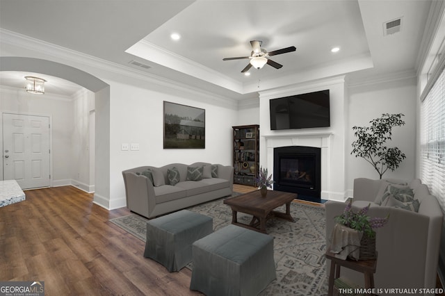 living area with visible vents, ceiling fan, dark wood-style floors, arched walkways, and a raised ceiling