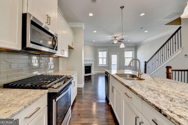 kitchen with a sink, appliances with stainless steel finishes, crown molding, decorative backsplash, and ceiling fan