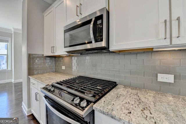 kitchen with stainless steel microwave, backsplash, gas stove, white cabinets, and light stone countertops