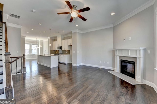 unfurnished living room with visible vents, ceiling fan, dark wood finished floors, ornamental molding, and a fireplace