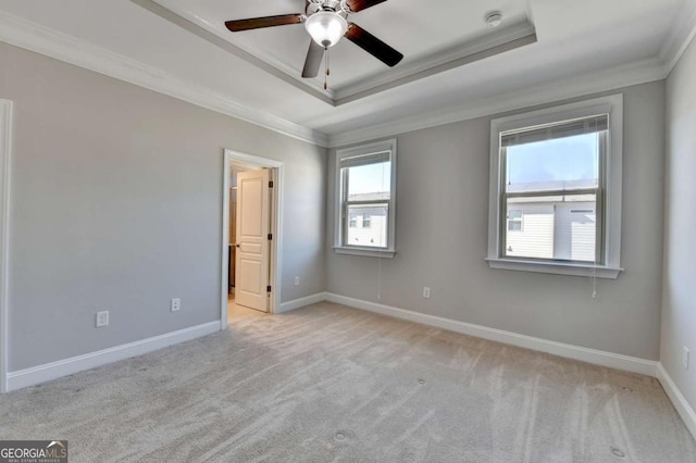 carpeted spare room with ceiling fan, a tray ceiling, baseboards, and ornamental molding