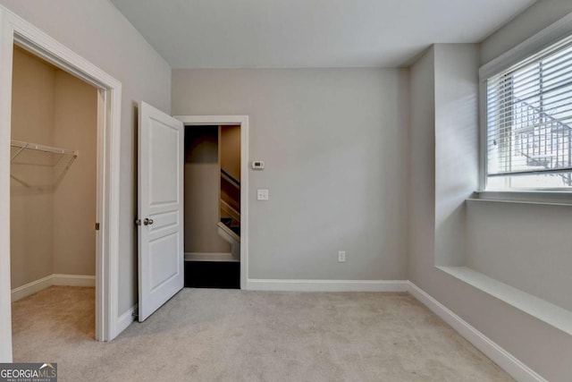 unfurnished bedroom with light carpet, a closet, a walk in closet, and baseboards