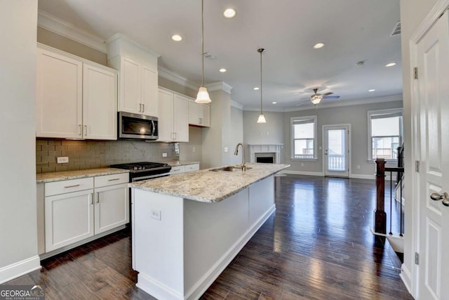 kitchen with a fireplace, a sink, decorative backsplash, ceiling fan, and appliances with stainless steel finishes