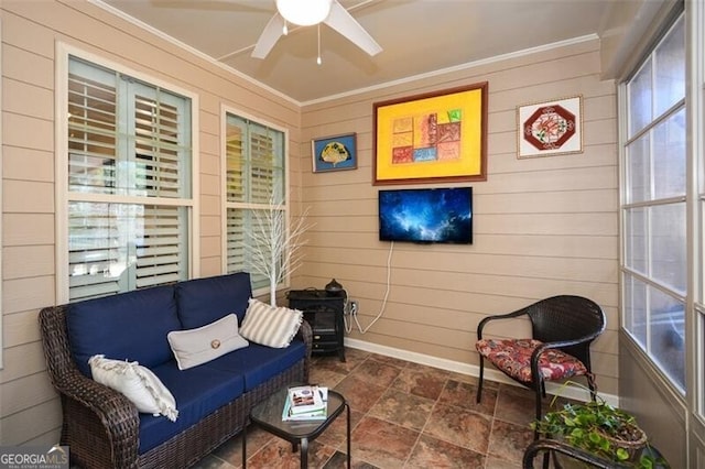 interior space featuring crown molding, baseboards, wood walls, stone finish floor, and a ceiling fan