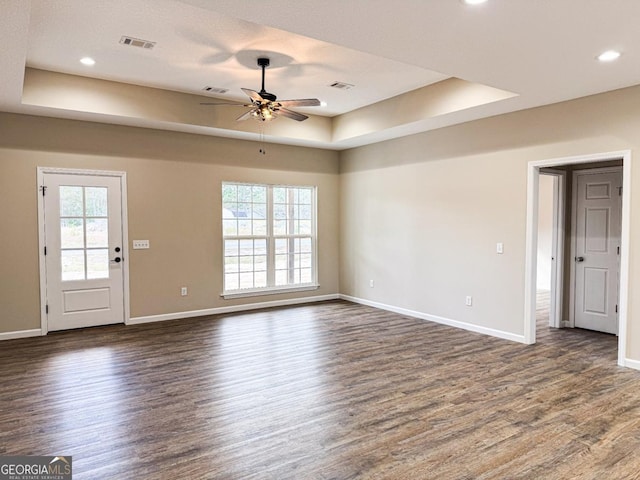 unfurnished living room featuring a raised ceiling, a ceiling fan, visible vents, and dark wood-type flooring