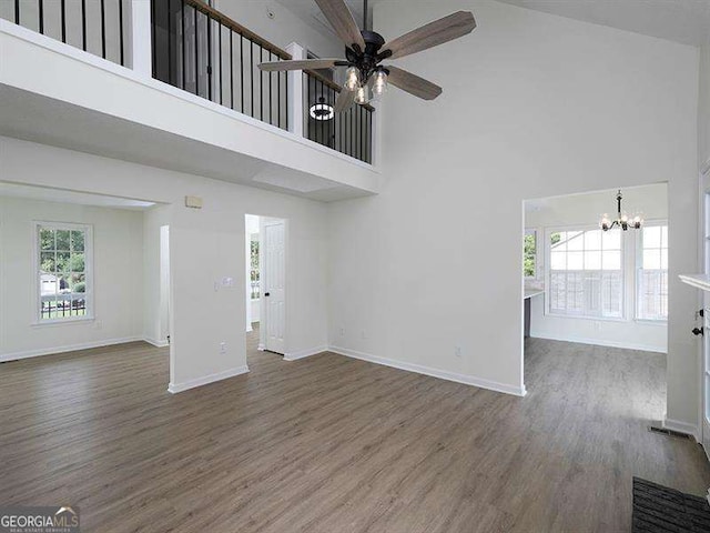 unfurnished living room featuring wood finished floors, a high ceiling, ceiling fan with notable chandelier, and baseboards