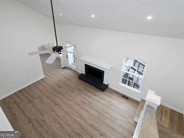 unfurnished living room featuring wood finished floors, baseboards, visible vents, lofted ceiling, and a fireplace with raised hearth