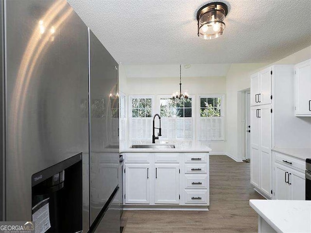 kitchen with light countertops, stainless steel refrigerator with ice dispenser, wood finished floors, white cabinetry, and a sink