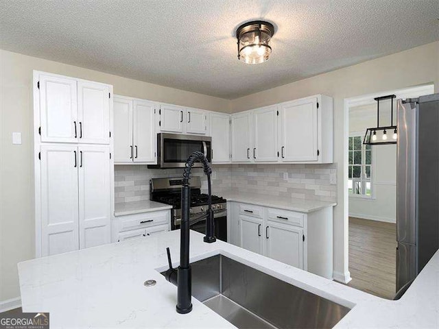 kitchen with a textured ceiling, backsplash, appliances with stainless steel finishes, and white cabinetry