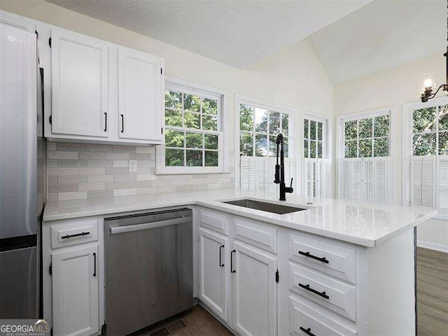 kitchen with a peninsula, lofted ceiling, a sink, stainless steel appliances, and white cabinetry