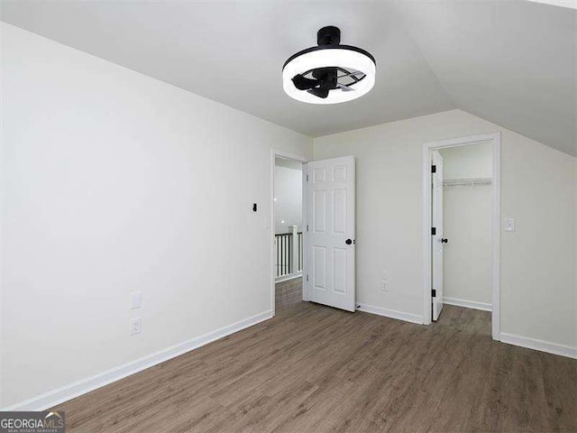 unfurnished bedroom featuring lofted ceiling, a spacious closet, wood finished floors, and baseboards