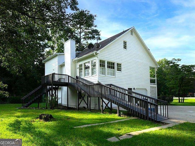 rear view of house featuring stairway, a garage, a chimney, and a lawn